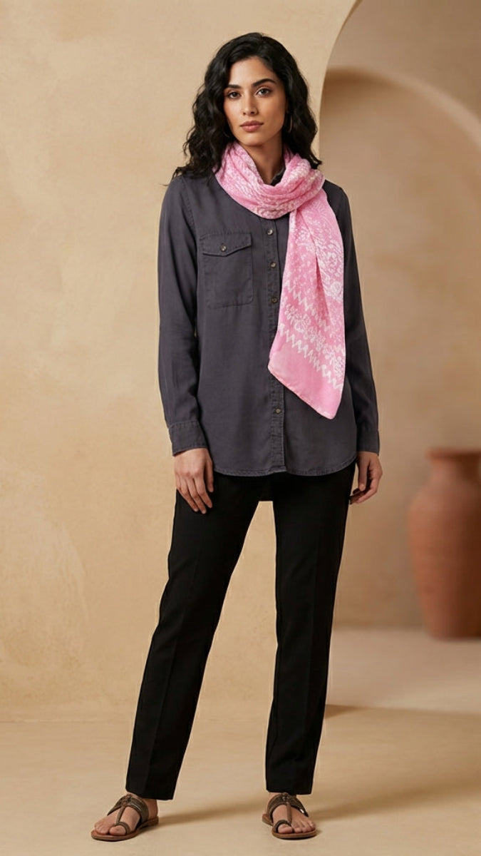 Woman wearing a gray shirt and black pants with a pink scarf, standing in a warm-toned room.