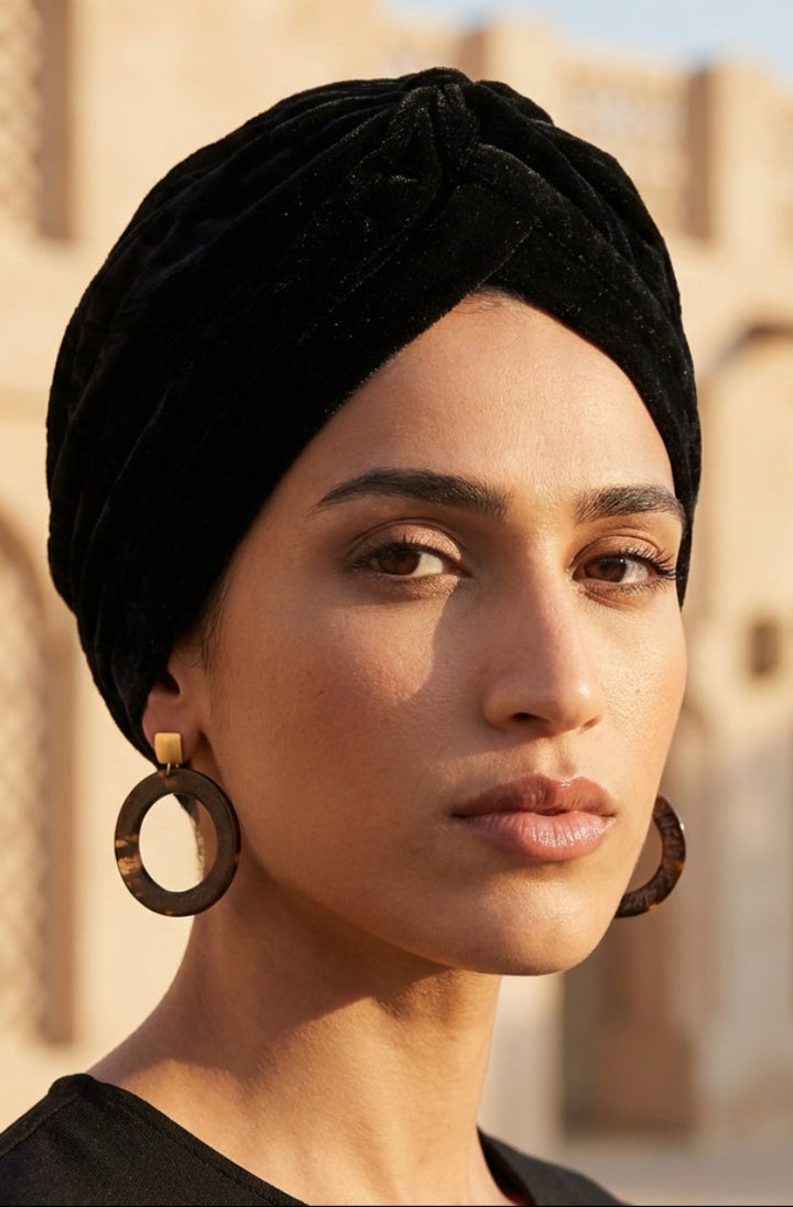 Woman wearing a black turban and large earrings with a blurred architectural background