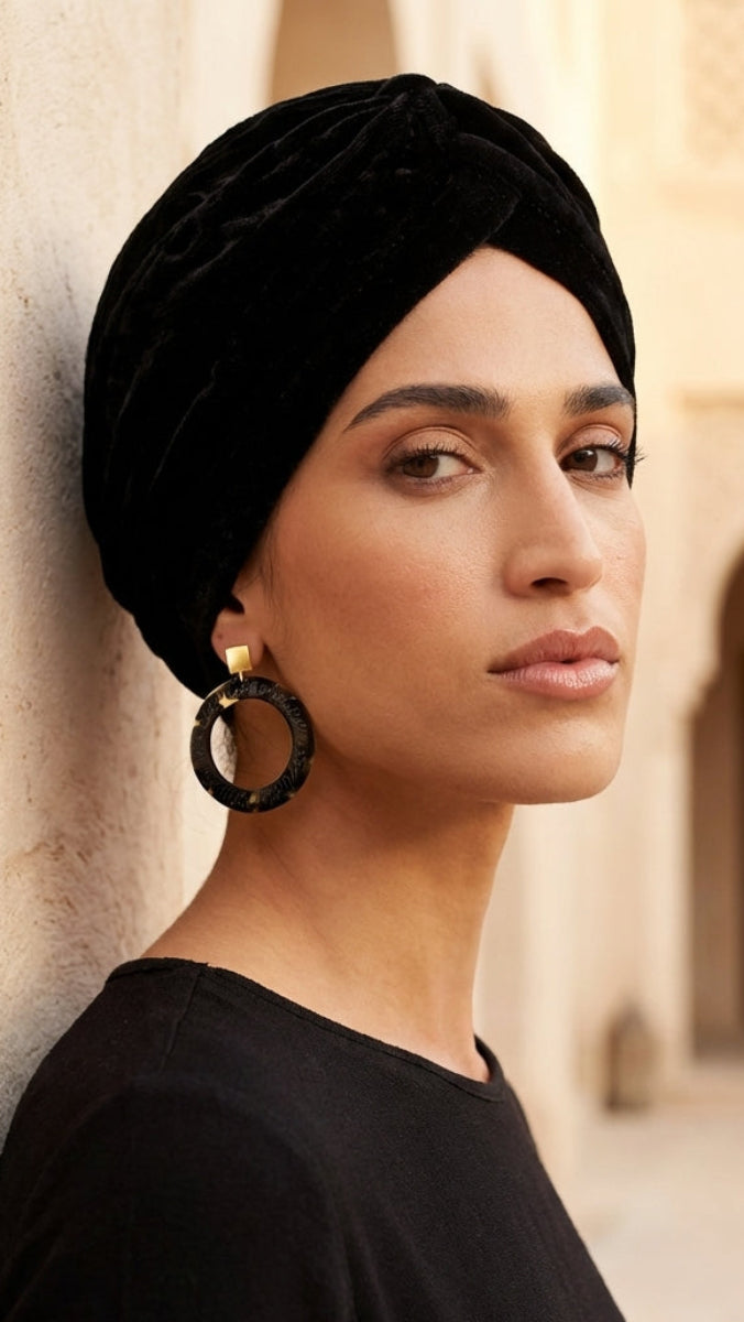 Woman wearing a black turban and black top in an outdoor setting with beige walls and arches.