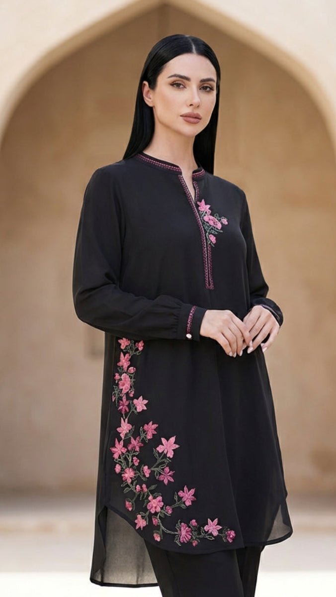 Woman wearing a black outfit with pink floral embroidery in front of an archway.