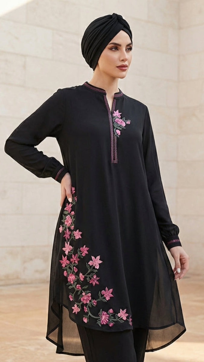 Woman wearing a black outfit with pink floral embroidery in front of a stone building.