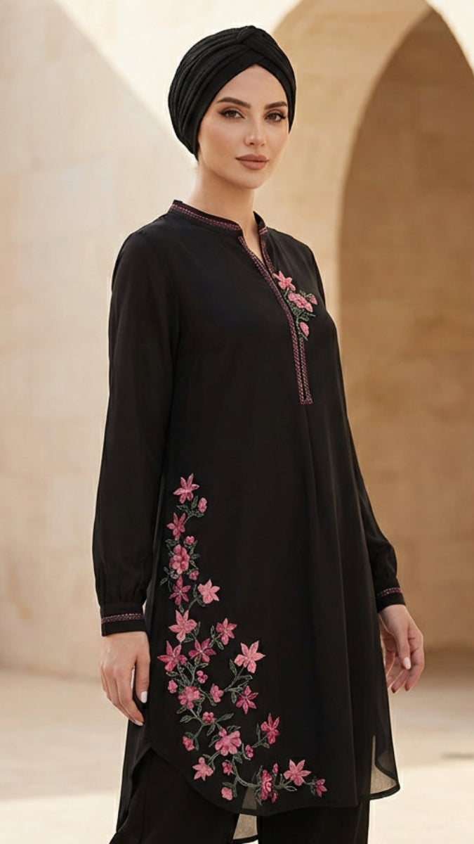 Woman wearing a black outfit with pink floral embroidery in an arched stone building setting