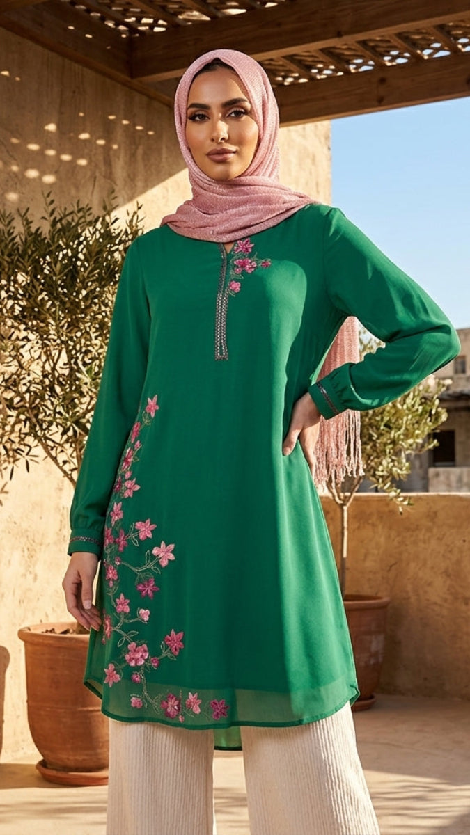 Woman wearing a green embroidered dress with a pink hijab standing outdoors.