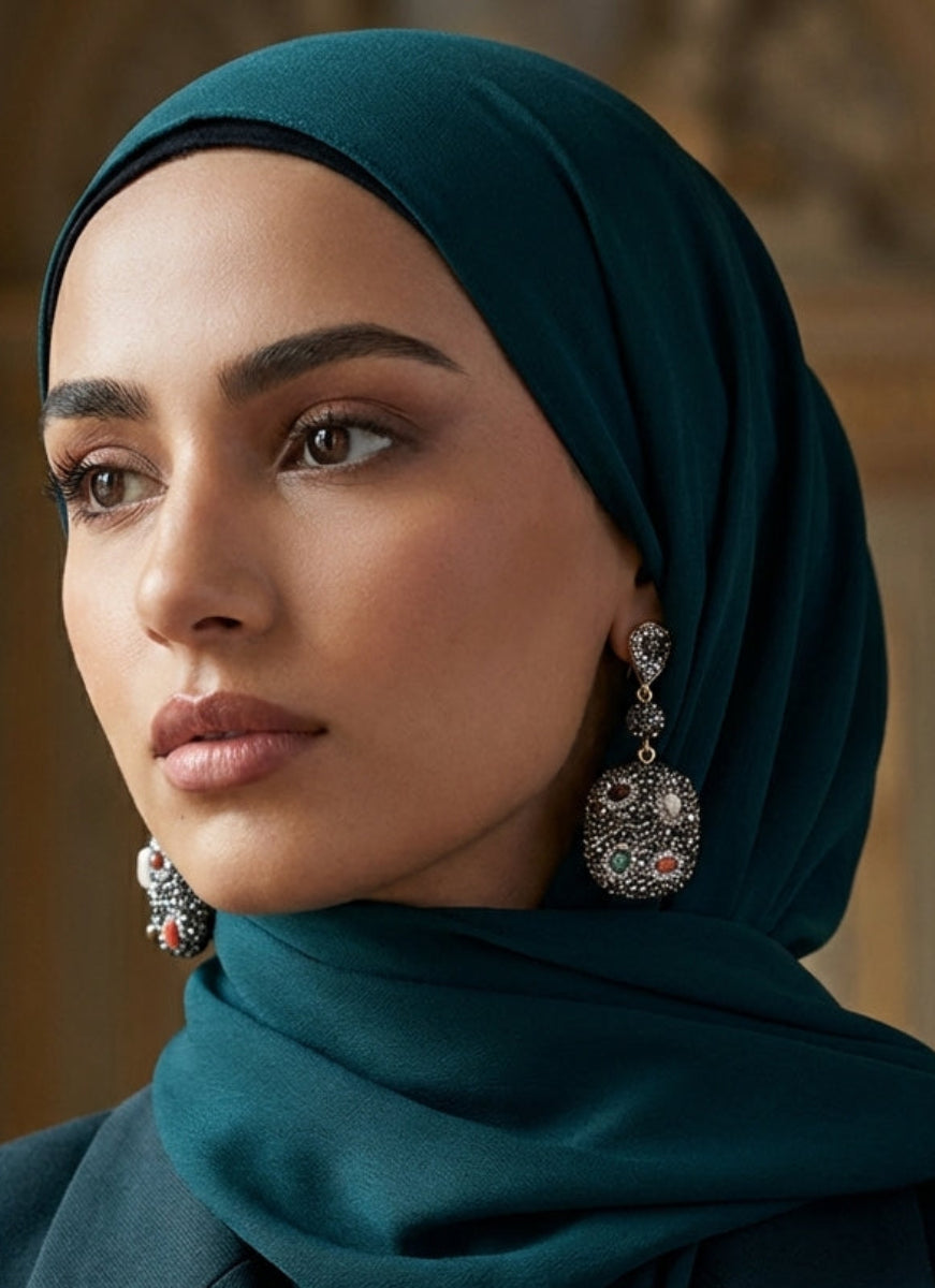 Woman wearing a teal hijab and earrings with a blurred background