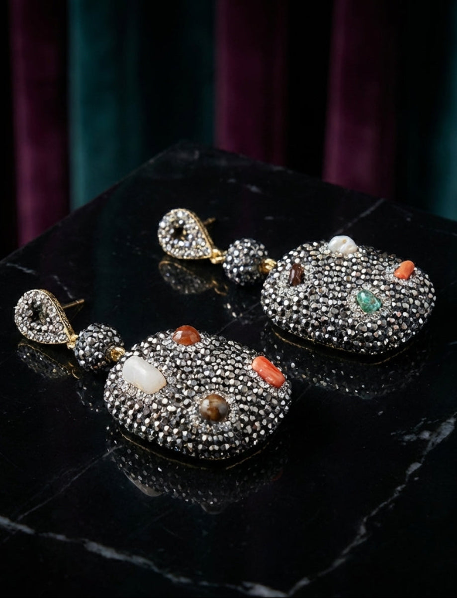 Ornate earrings with gemstones on a dark surface