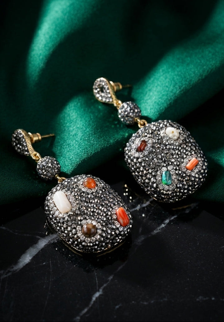 Pair of ornate earrings with gemstones on a green fabric background