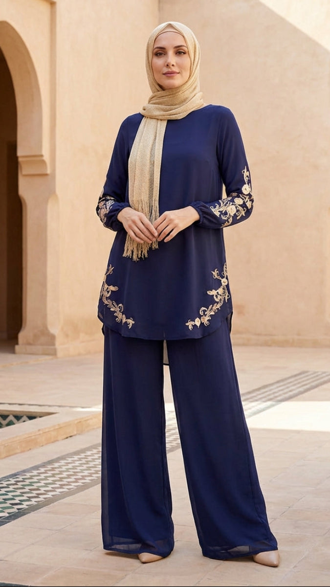 Woman in a navy blue outfit with gold embroidery standing in a sunlit courtyard.