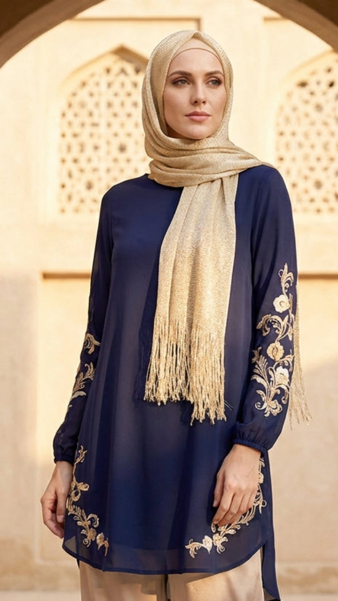 Woman wearing a blue embroidered dress with a beige hijab standing in an archway.