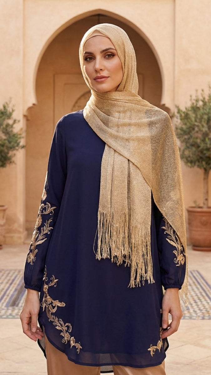 Woman wearing a navy blue top with gold embroidery and beige hijab in a decorative outdoor setting.