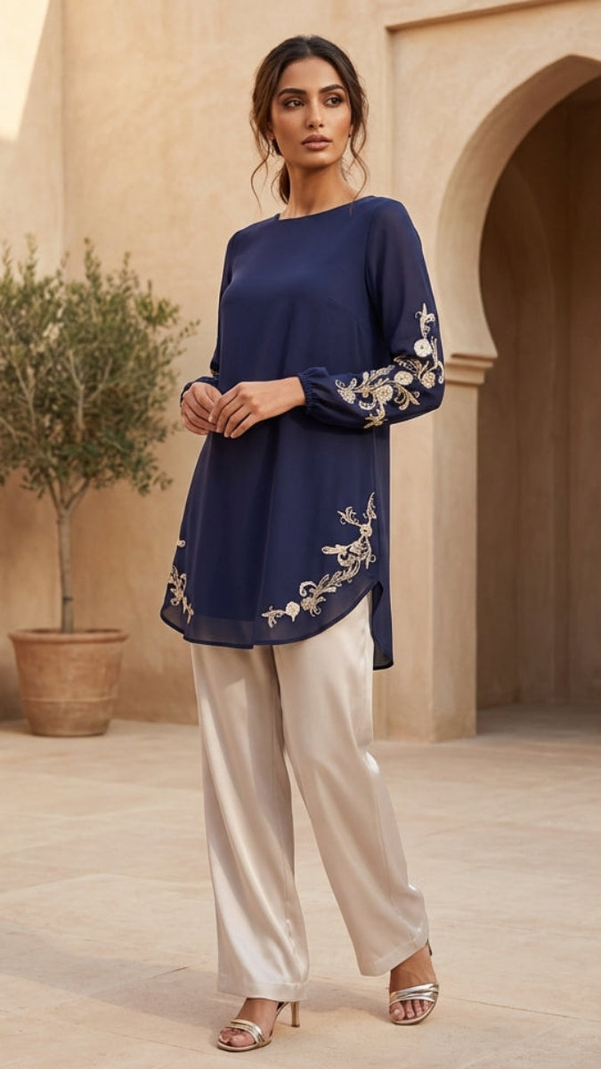 Woman wearing a navy blue top with white embroidery and light-colored pants in an outdoor setting.