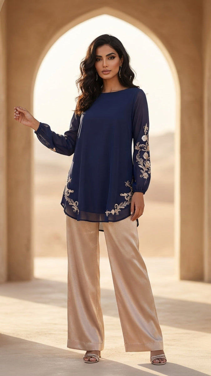 Woman in a blue top and beige pants standing in a sunlit archway.