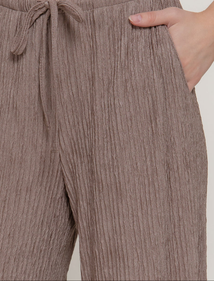 Brown ribbed pants with a tie waist on a plain background