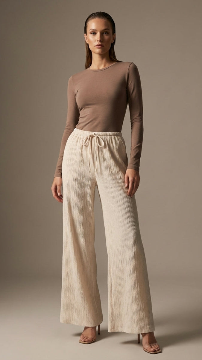 Woman wearing a brown top and beige wide-leg pants against a plain background