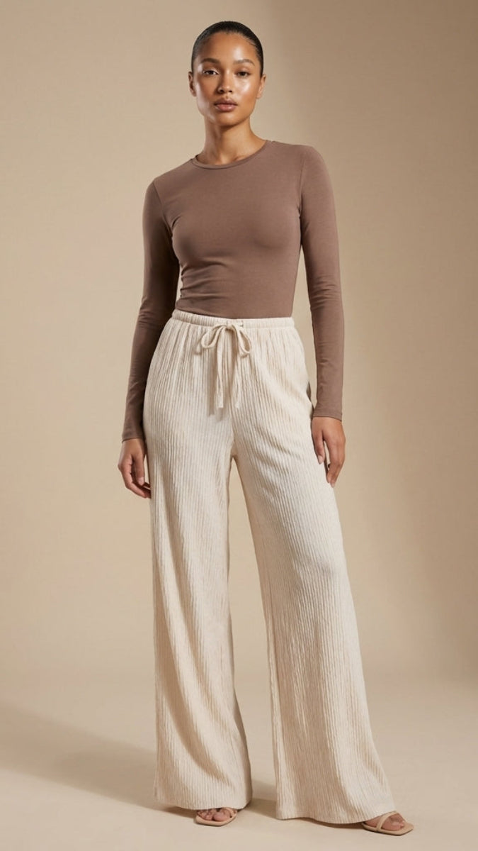 Woman wearing a brown long-sleeve top and cream wide-leg pants against a beige background