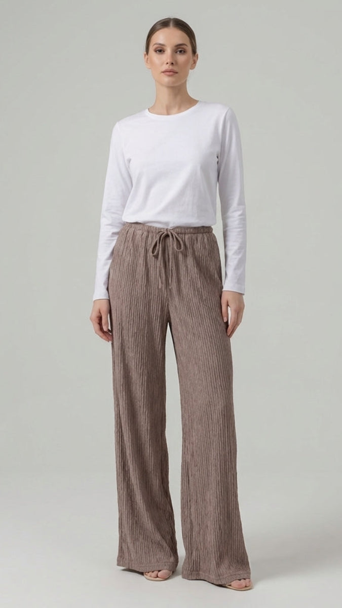 Woman wearing a white long-sleeve top and brown wide-leg pants on a gray background