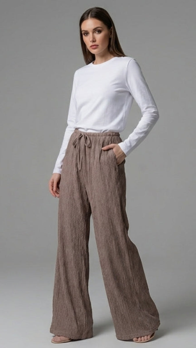 Woman wearing a white top and brown wide-leg pants on a gray background