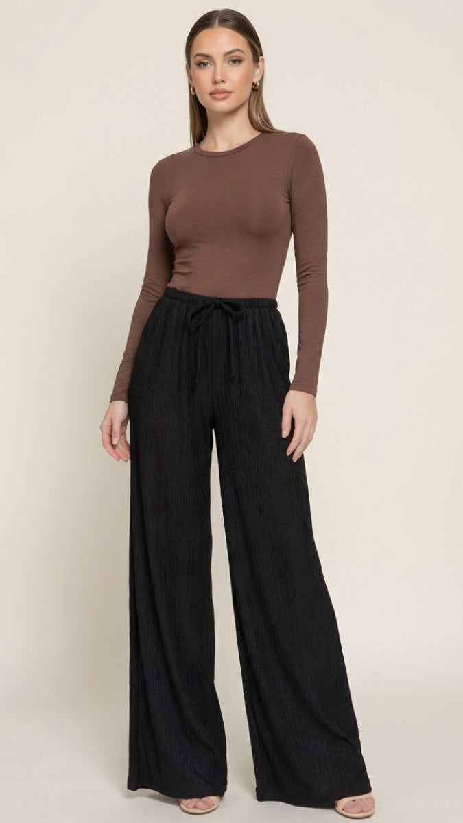 Woman wearing a brown long-sleeve top and black wide-leg pants on a beige background