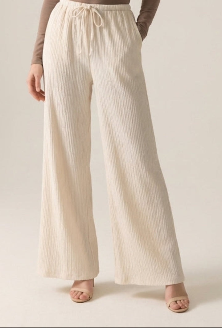 Woman wearing a brown long-sleeve top and cream wide-leg pants on a plain background