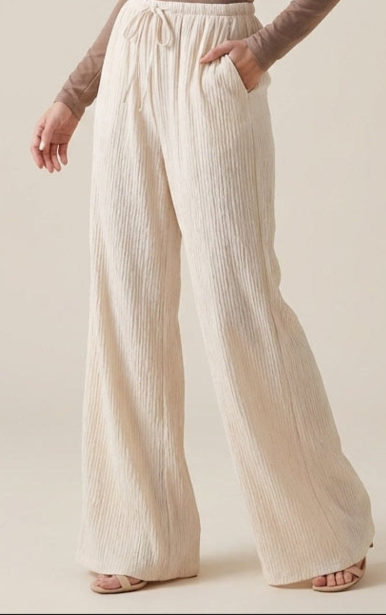 Woman wearing a brown long-sleeve top and white wide-leg pants against ...