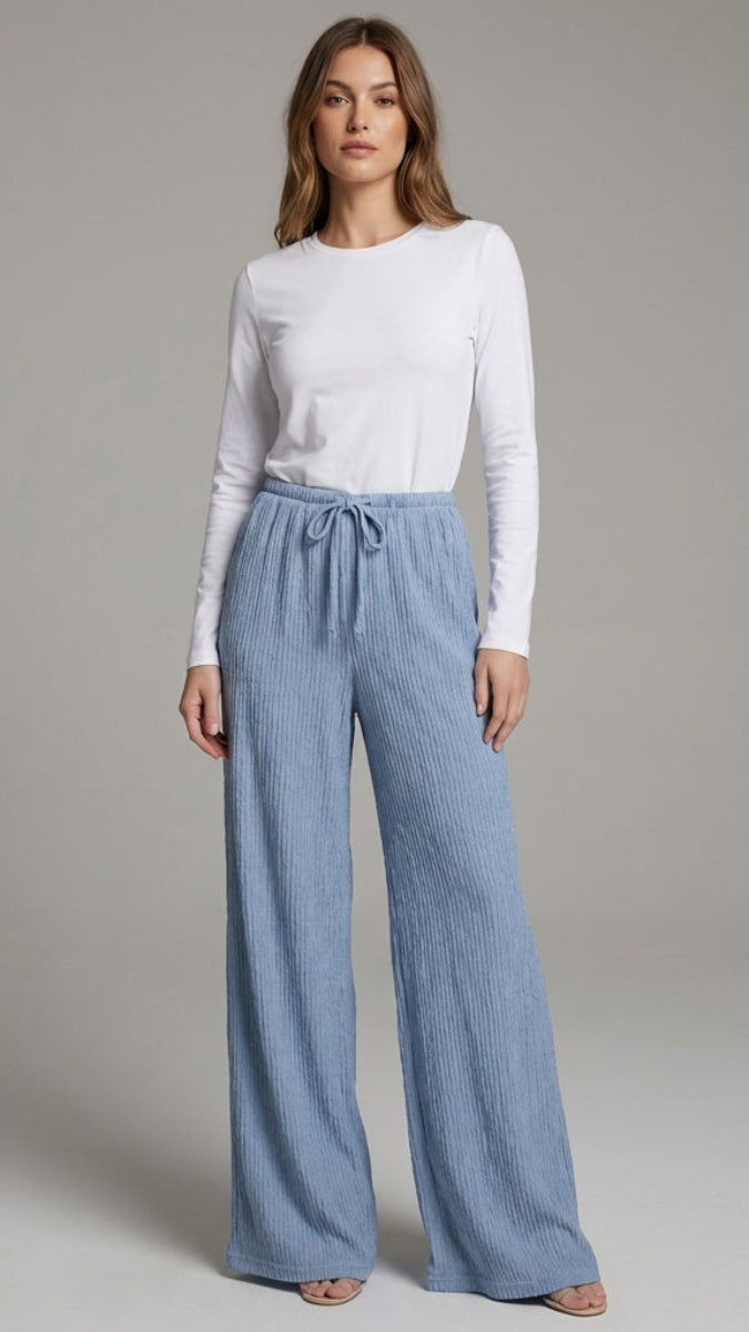 Woman wearing a white long-sleeve top and blue wide-leg pants on a gray background