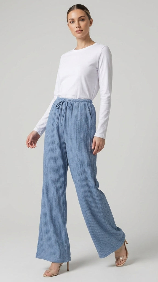 Woman wearing a white top and blue pants on a plain background