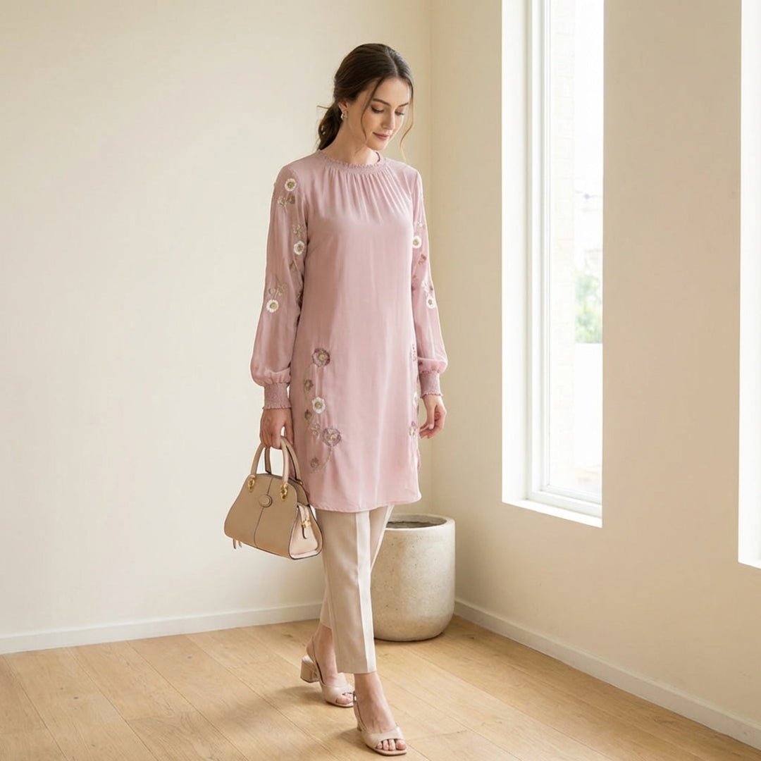 Woman in a pink dress holding a beige handbag in a room with a window and plant.