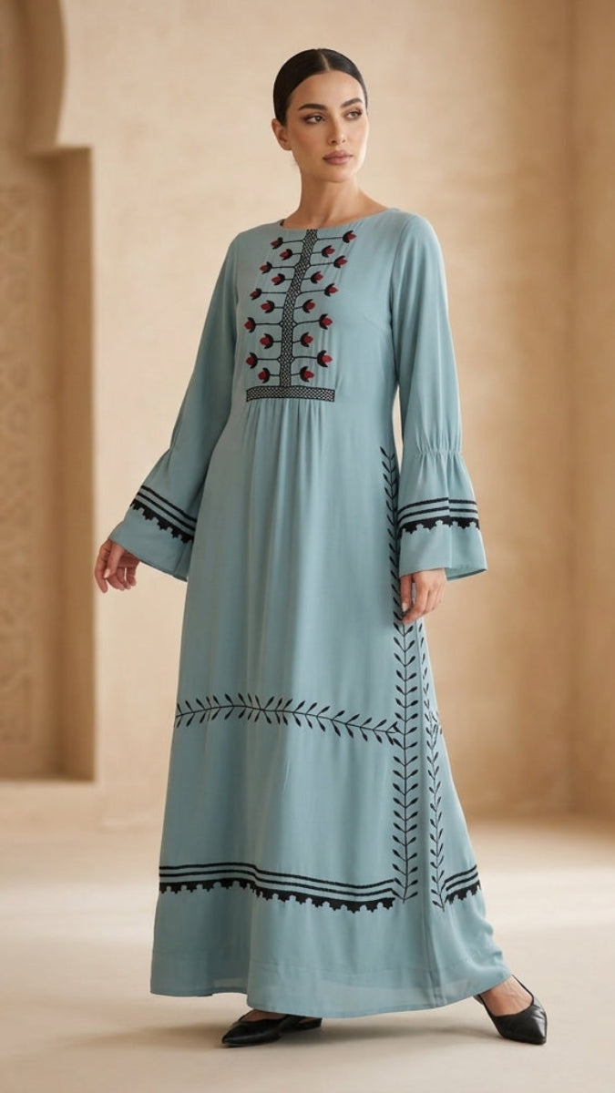 Woman wearing a long, light blue embroidered dress against a neutral background