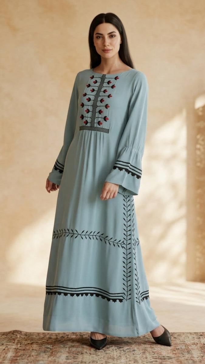 Woman wearing a long, light blue dress with embroidery against a beige background