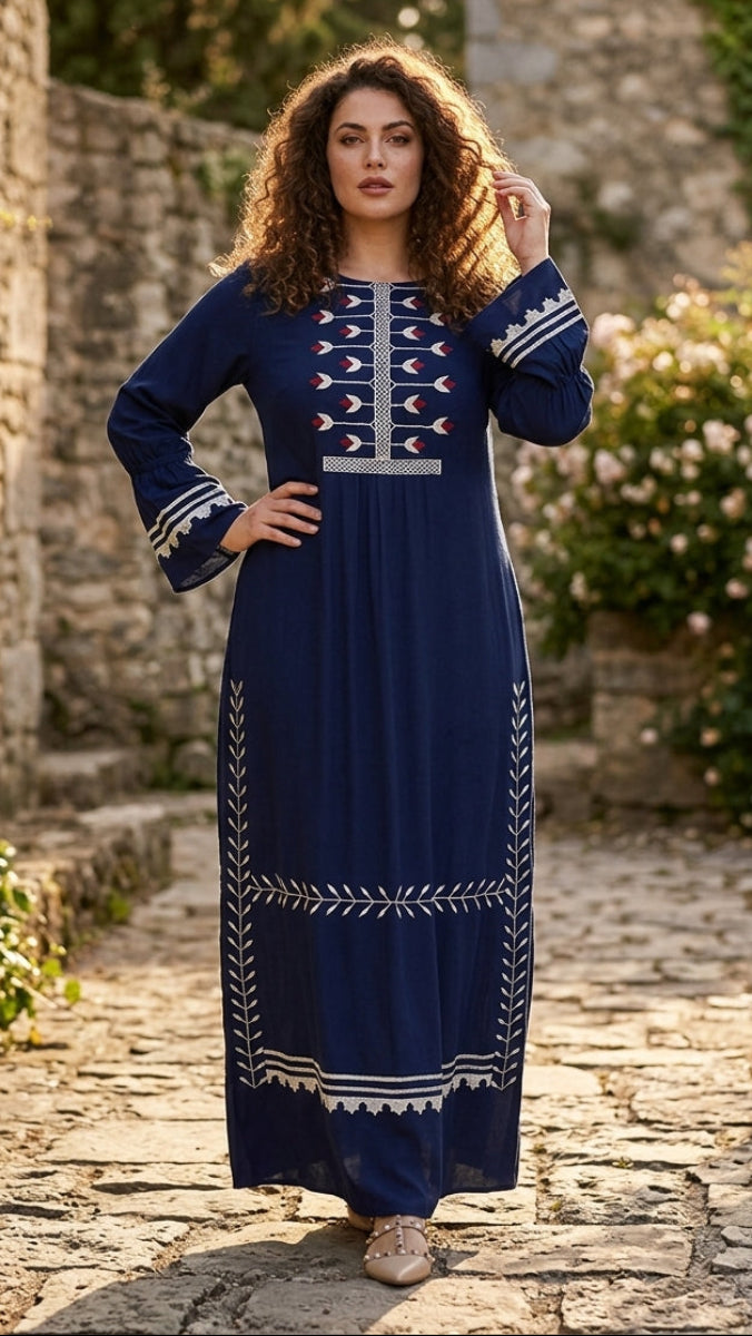 Woman in a blue dress with white patterns standing on a stone path with greenery.