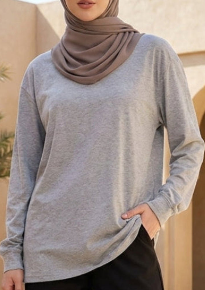 Woman wearing a hijab and standing in a sunlit courtyard with palm trees and arches.