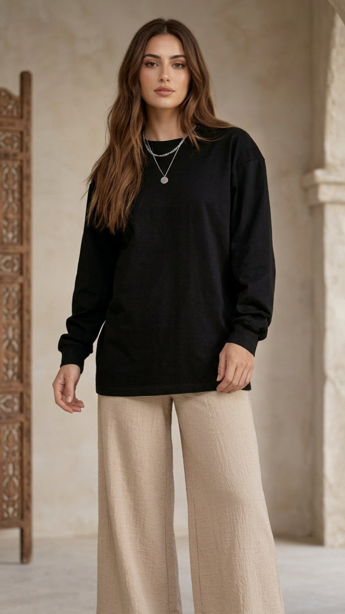 Woman wearing a black sweater and beige pants standing in a decorative interior setting.