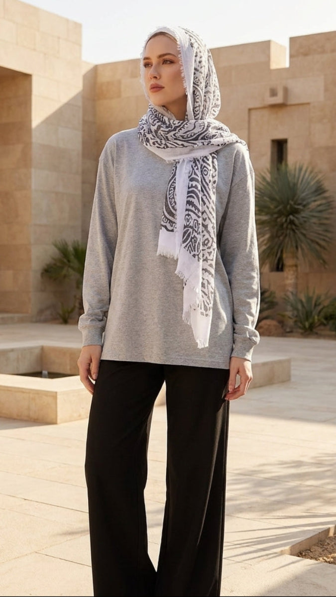 Woman wearing a gray sweater and black pants with a patterned scarf in an outdoor setting.