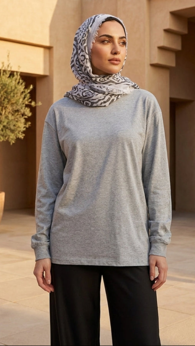 Woman wearing a gray long-sleeve top and black pants with a patterned headscarf in an outdoor setting.