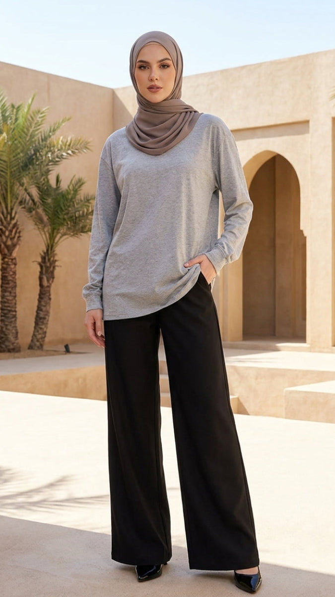 Woman wearing a hijab and standing in a sunlit courtyard with palm trees and arches.