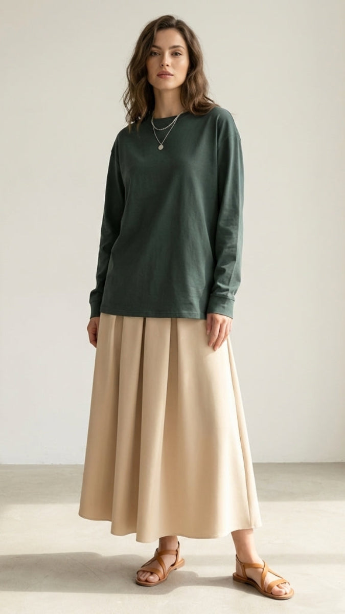 Woman wearing a green long-sleeve top and beige skirt against a plain background