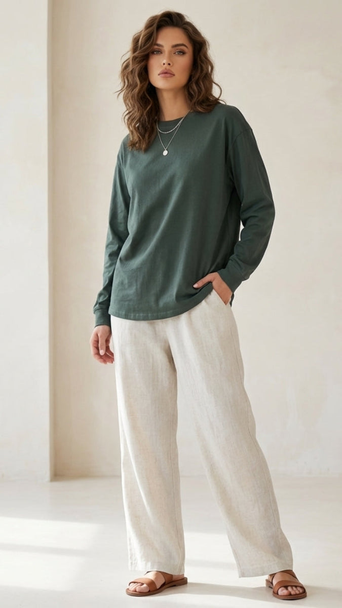Woman wearing a green sweater and white pants against a neutral background