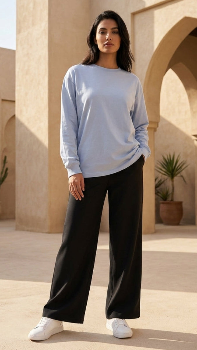 Woman standing in a sunlit architectural setting with arches and plants.