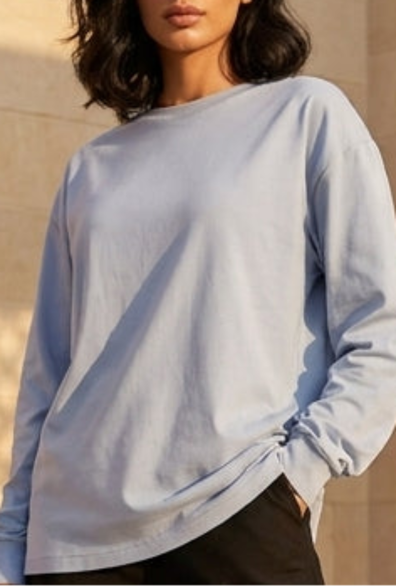 Woman standing in a sunlit architectural courtyard wearing a light blue sweater and black pants.