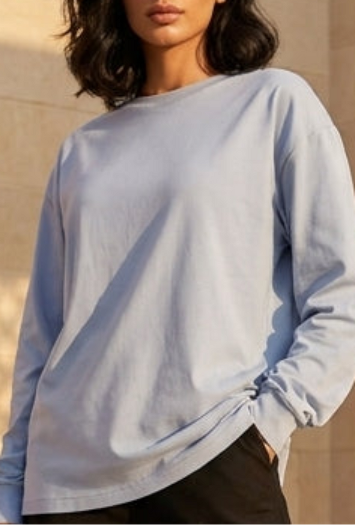 Woman standing in a sunlit architectural courtyard wearing a light blue sweater and black pants.
