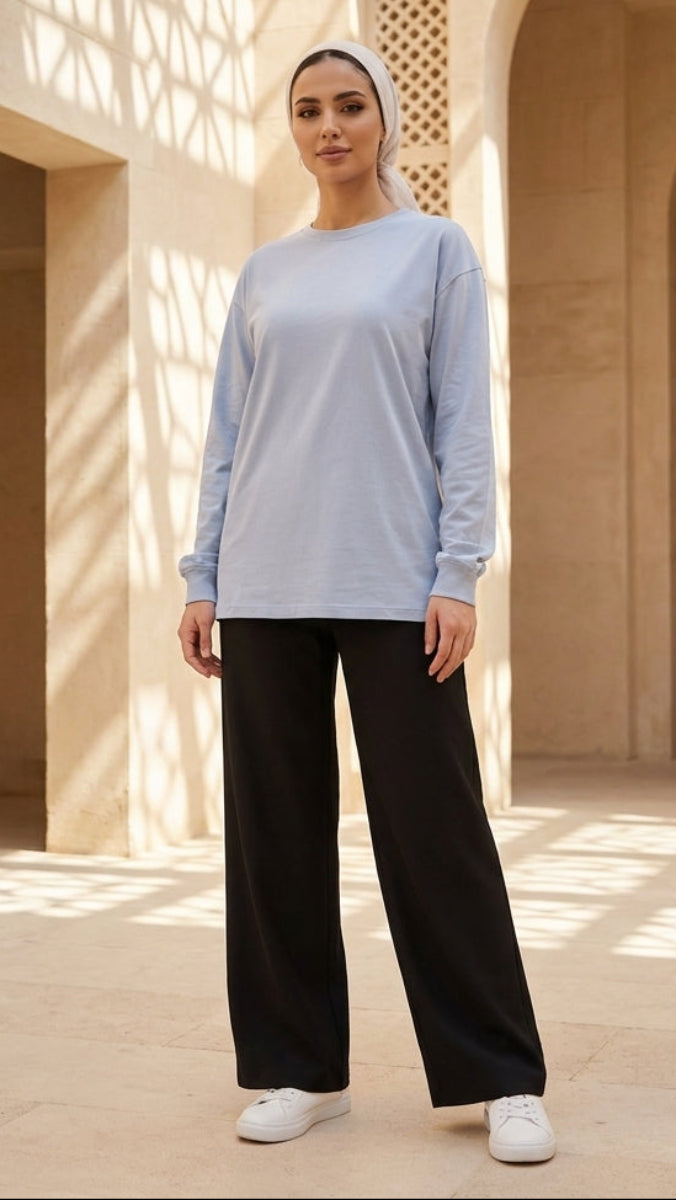 Woman in light blue top and black pants standing in a sunlit architectural setting
