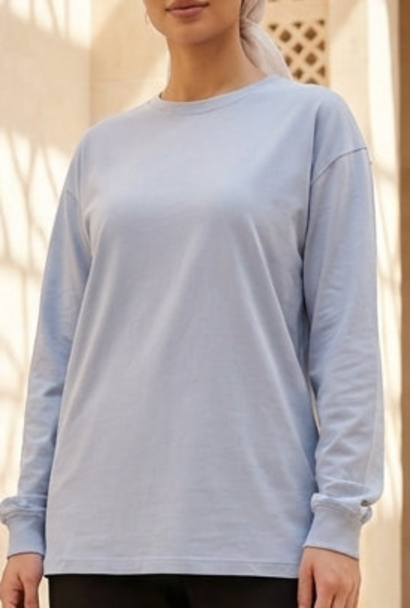 Woman in light blue top and black pants standing in a sunlit architectural setting