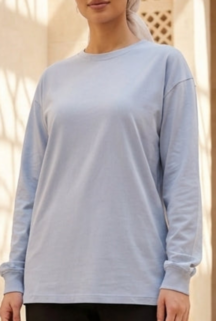 Woman in light blue top and black pants standing in a sunlit architectural setting