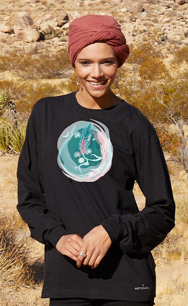 Woman standing in a desert landscape wearing a black long-sleeve shirt with a graphic design and black leggings.