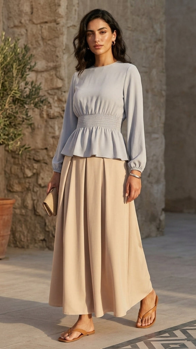 Woman in a light blue top and beige skirt standing in front of a stone wall.