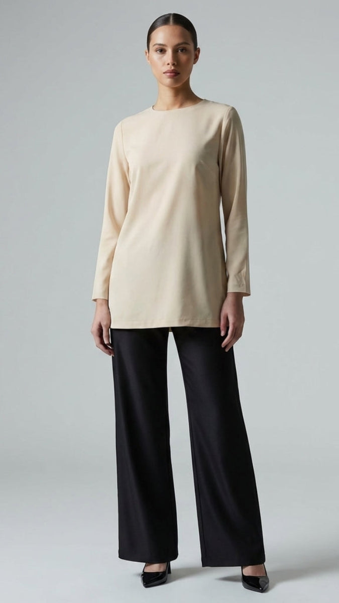Woman wearing a beige top and black pants on a gray background