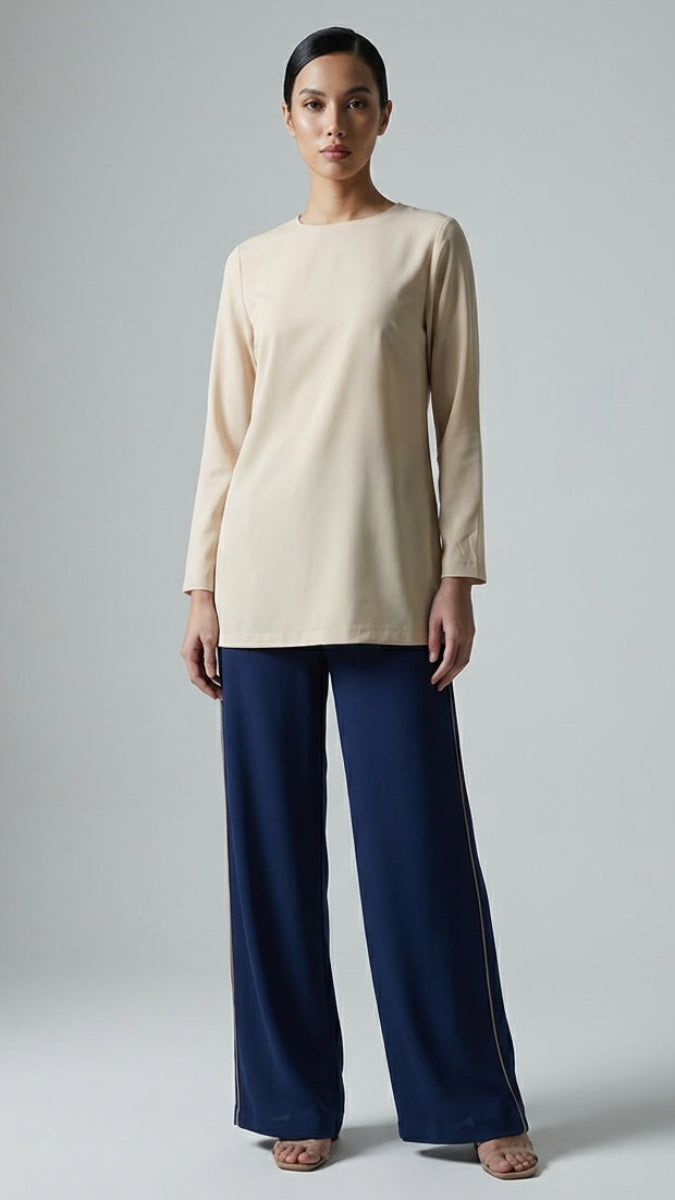 Woman wearing a beige top and navy pants on a gray background