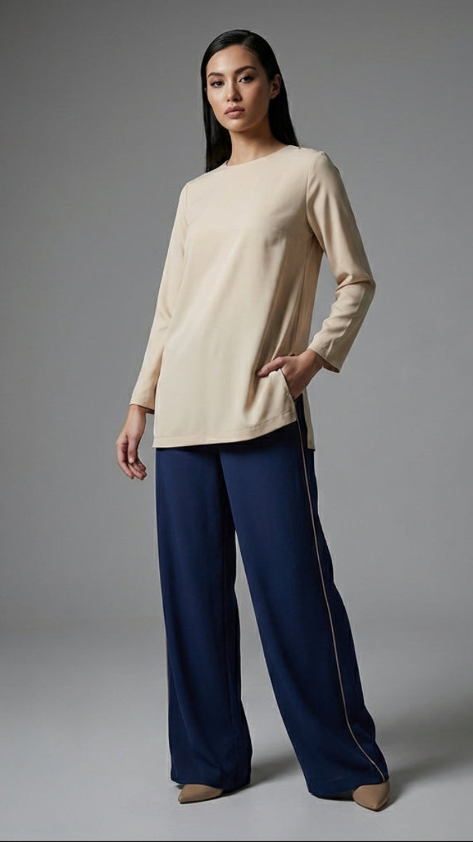 Woman wearing a beige top and blue pants against a gray background