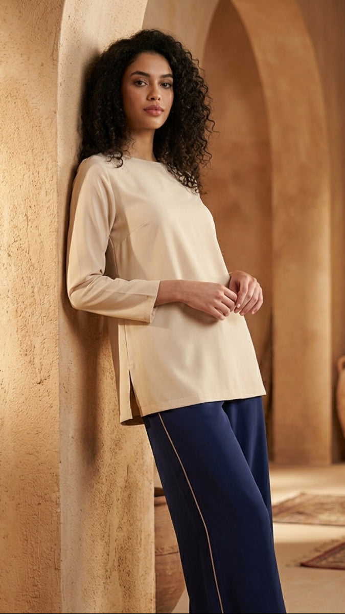 Woman in a beige top and blue pants standing against a textured wall with decorative vases.