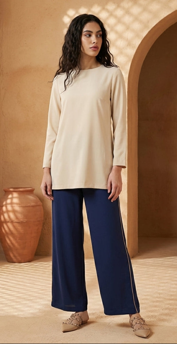 Woman in beige top and blue pants standing in a warm-toned room with an arched doorway.