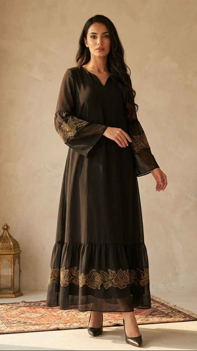 Woman in a black dress with gold embroidery standing in a room with a window and decorative elements.